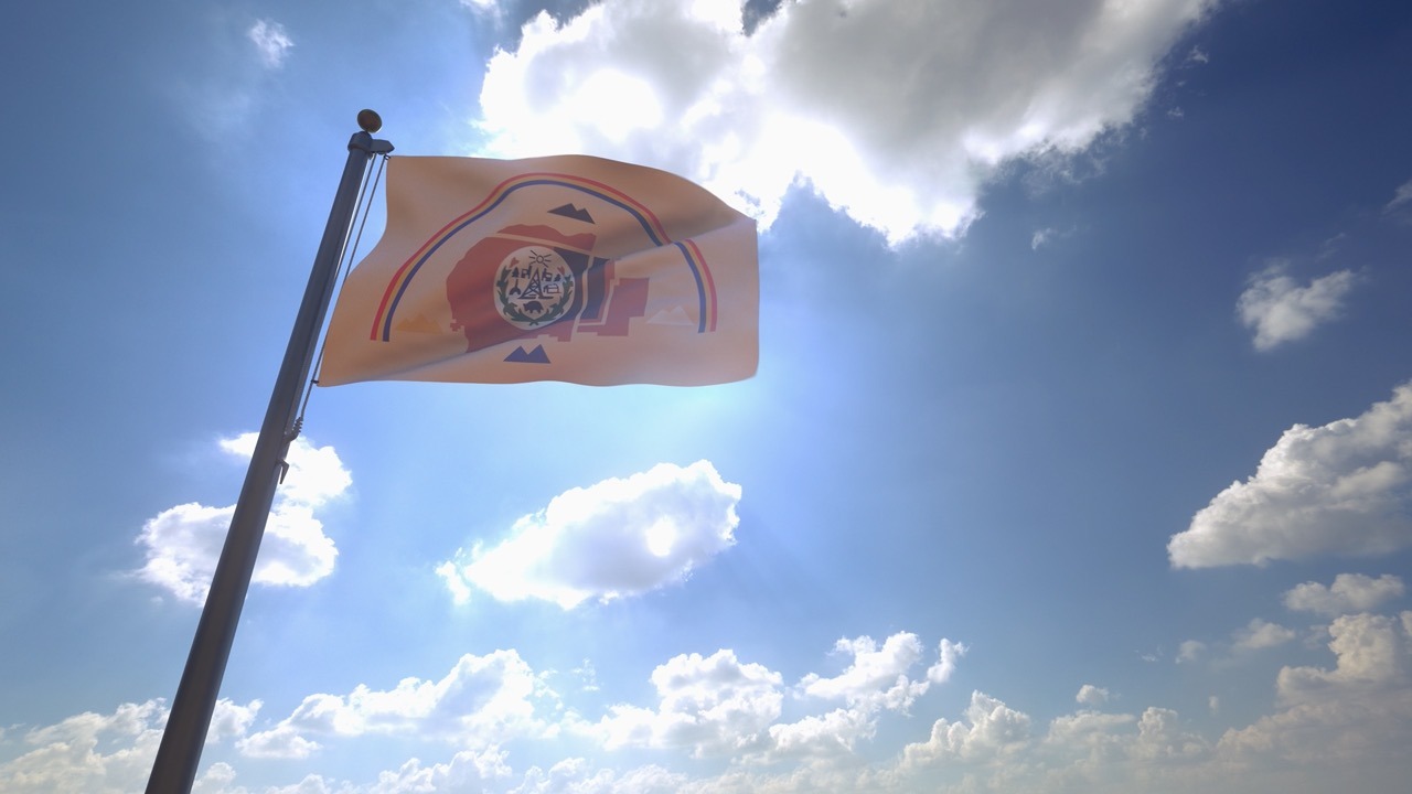 Navajo Nation flag waving on a flagpole against a blue sky, representing tribal government document exchange