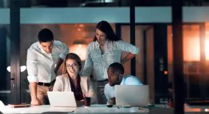 Team gathered around laptops in an office at night preparing for a fax compliance review