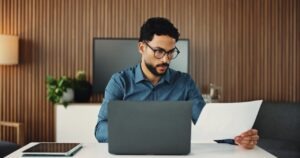 IT manager reviewing budget paperwork on a laptop while weighing fax IT budget cuts