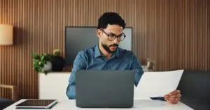 IT manager reviewing budget paperwork on a laptop while weighing fax IT budget cuts